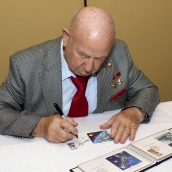 Alexei Leonov signing the first day cover depicting him making the first space walk