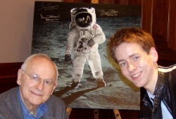 Alan Bean and Ciaran Brown in front of a large photograph  signed by Alan Bean, Gene Cernan and Buzz Aldrin